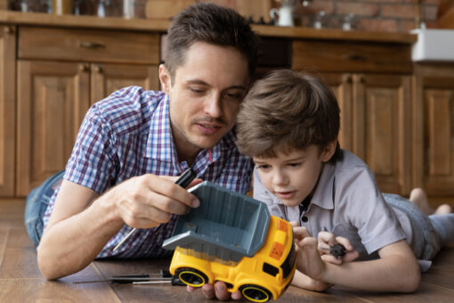 Caring young Caucasian father and little 6s son have fun fixing toy car at home together. Loving dad teach small boy child repair automobile, feel playful relax on family leisure weekend.